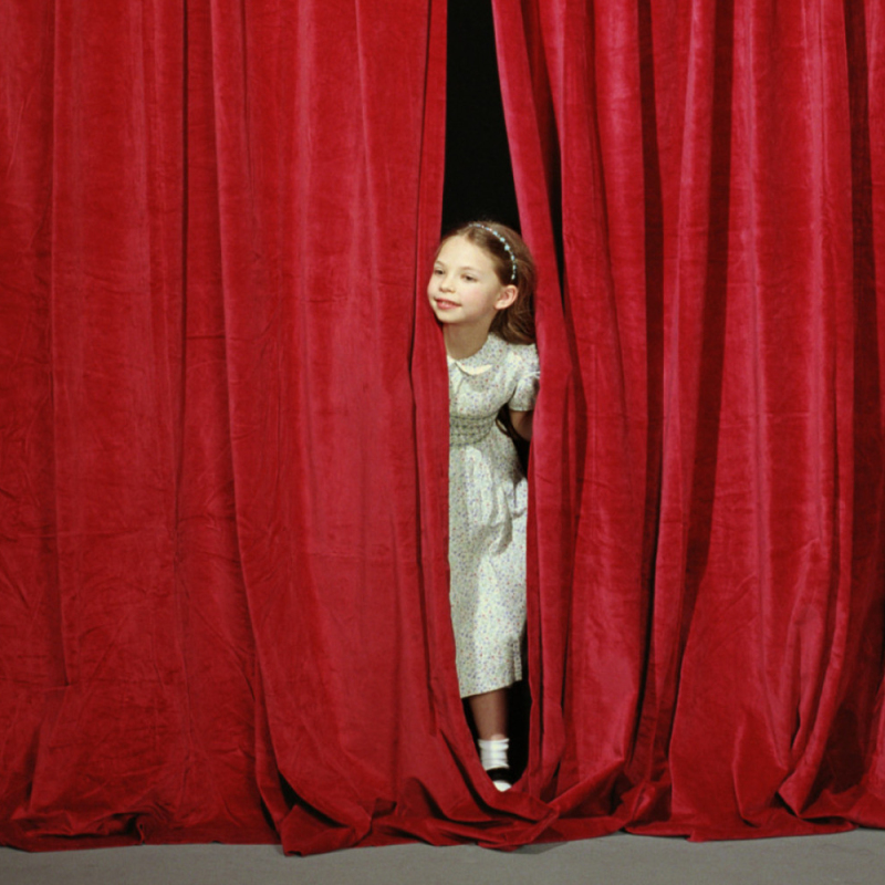 Girl (7-9) looking out from behind stage curtain